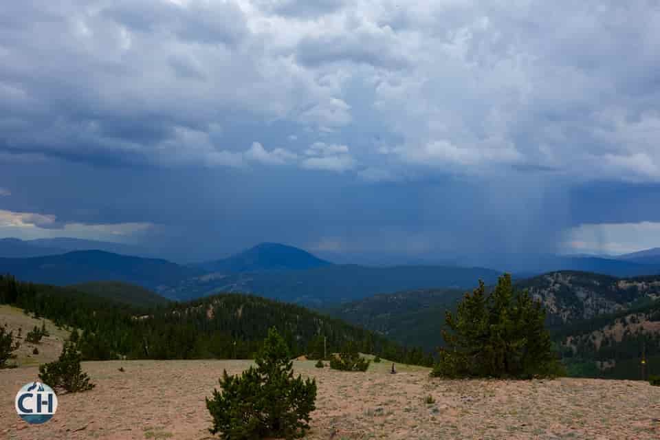 rain falls over a distant mountain as viewed from another mountain trail