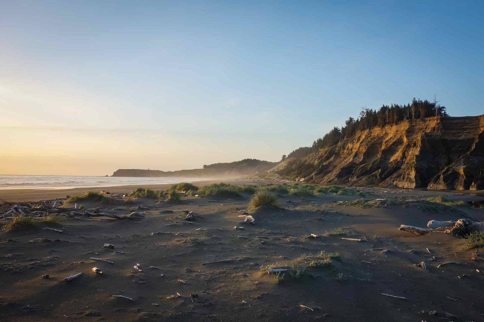 a perfect pacific ocean sunset over the oregon coast with white sandy beaches, beachwood, and abrupt cliffs.