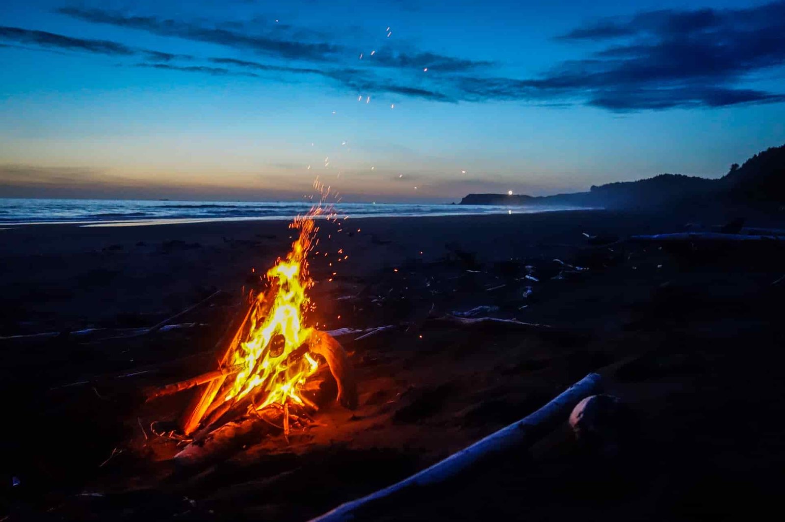 Beach campfire on the oregon coast trail just after sunset with rich blue and orange skies