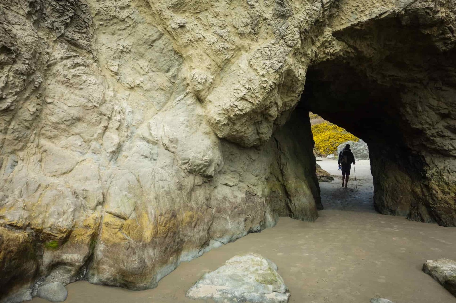 a backpacker on the oregon coast trail walks under a natural bridge.