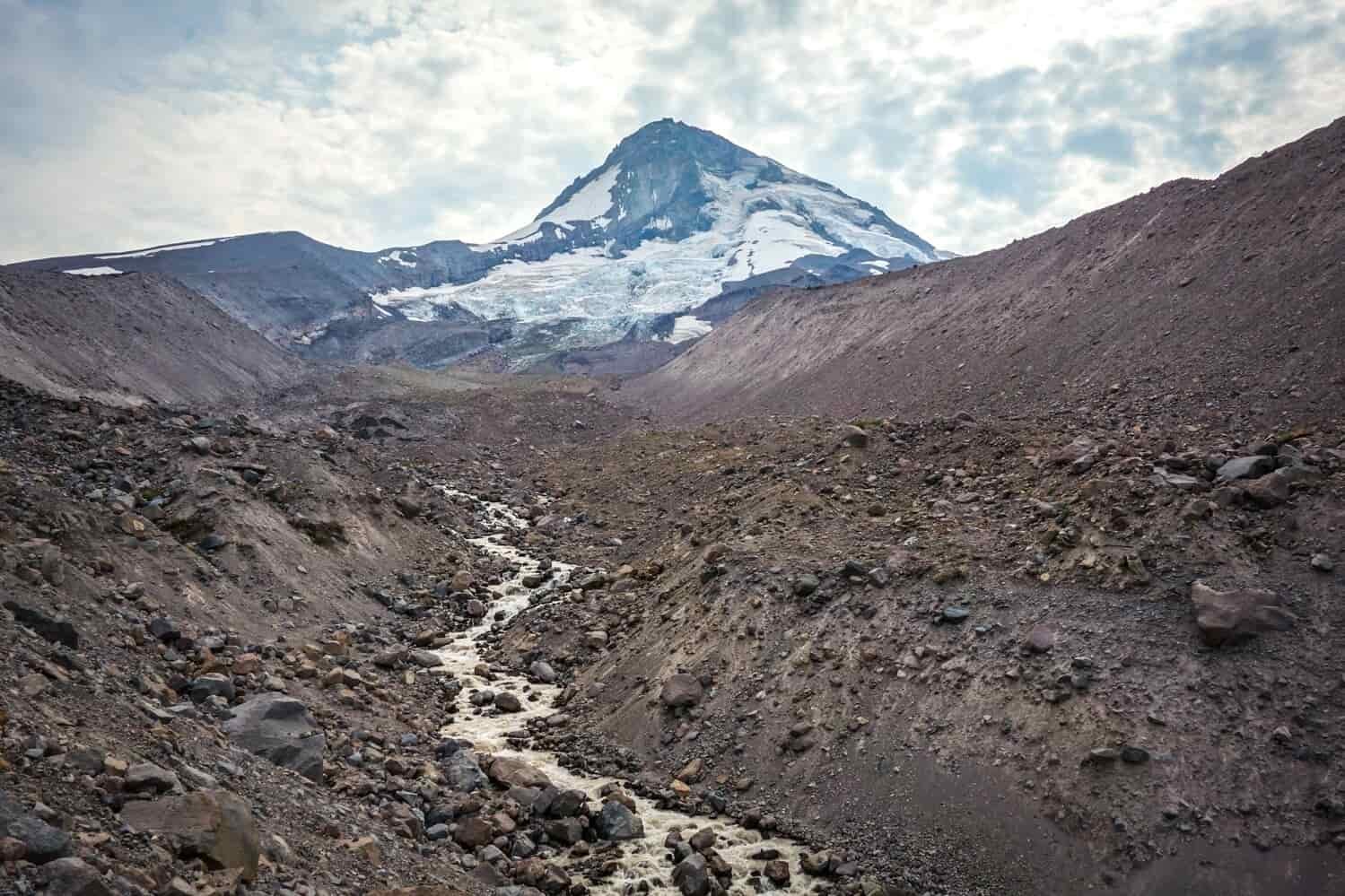 small creek filled with cloudy glacial runoff on below the snow capped peak of mt. hood.