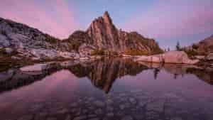 sunrise over a granite spire with a lake reflecting the sky