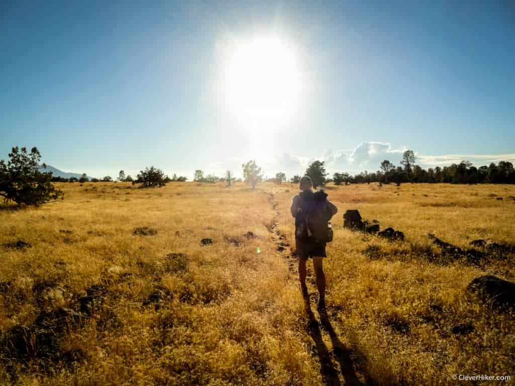 A hiker walks down a faint trail through a brown grassland