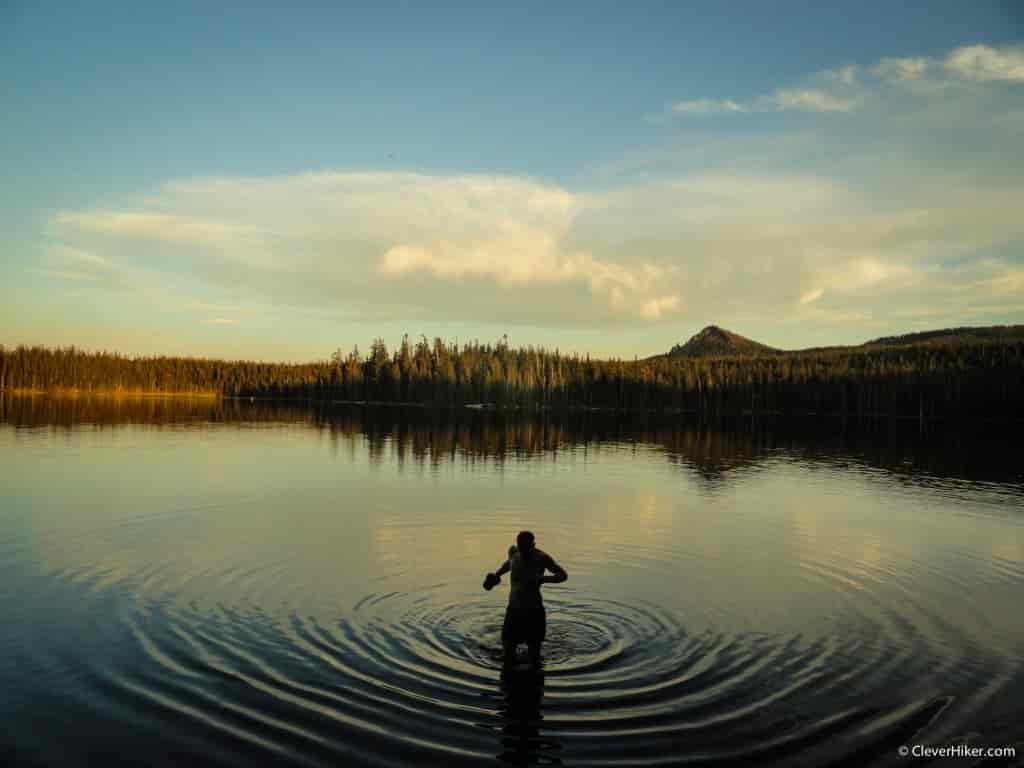 A hiker walks thigh-deep through a backcountry lake