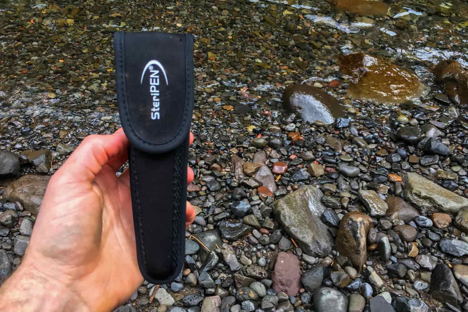 a backpacker holding the steripen ultra uv water purifier in its case next to wet river rocks
