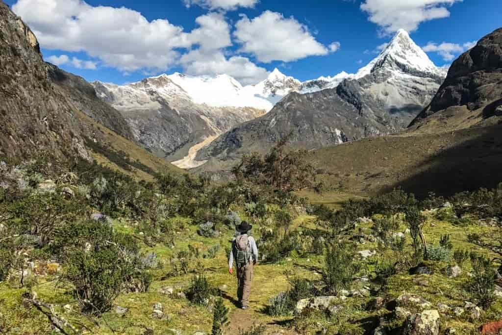 A hiker wears a cowboy hat while walking through a green valley on the Santa Cruz Trek