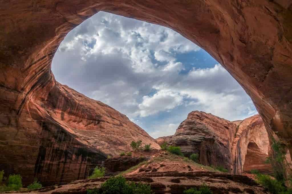 a look through a large sandstone arch to the blue ski with clouds