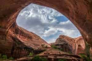 a look through a large sandstone arch to the blue ski with clouds