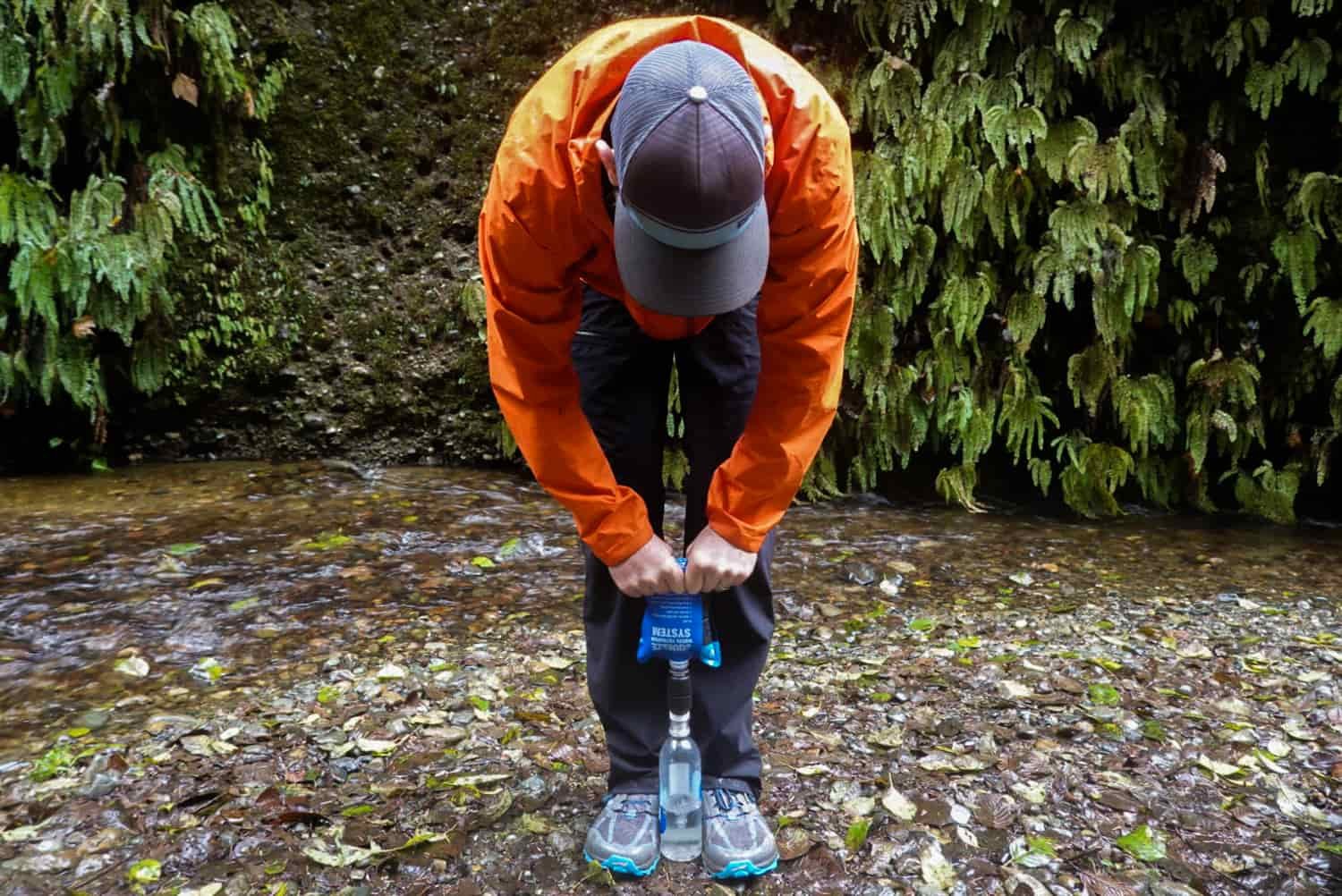 backpacker squeezes water out of a pouch and through a filter into a water bottle next to a stream