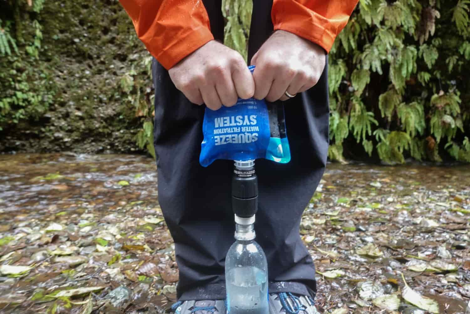 close up of a backpacker rolling and squeezing the pouch so water gets filtered before going into a water bottle.