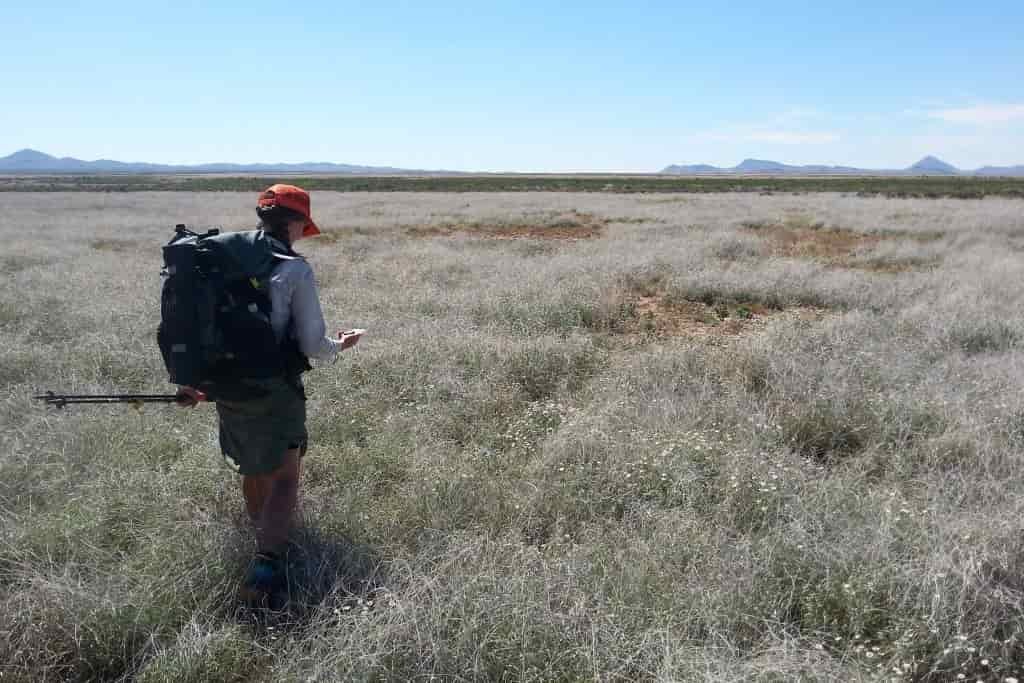 A female hiker looks down at her compass while walking across a desert plain
