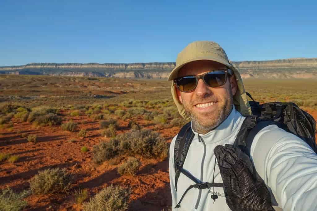 A hiker smiles while wearing a sun hat and sun hoody in the desert