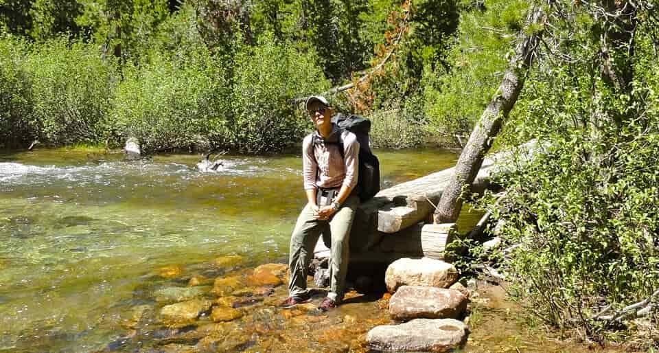 a women sits on a rock in water with a lamenting look on her face