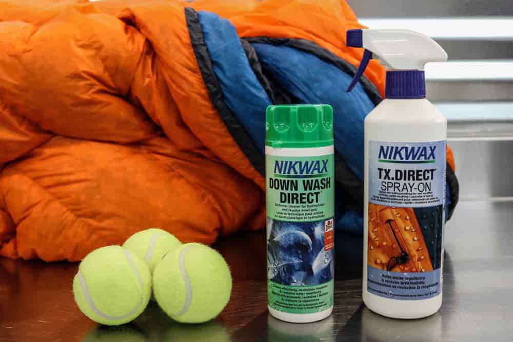 Shot of a table top with a sleeping bag, three tennis balls, a bottle of Nikwax Down Wash Direct, and a spray bottle of Nikwax TX Direct