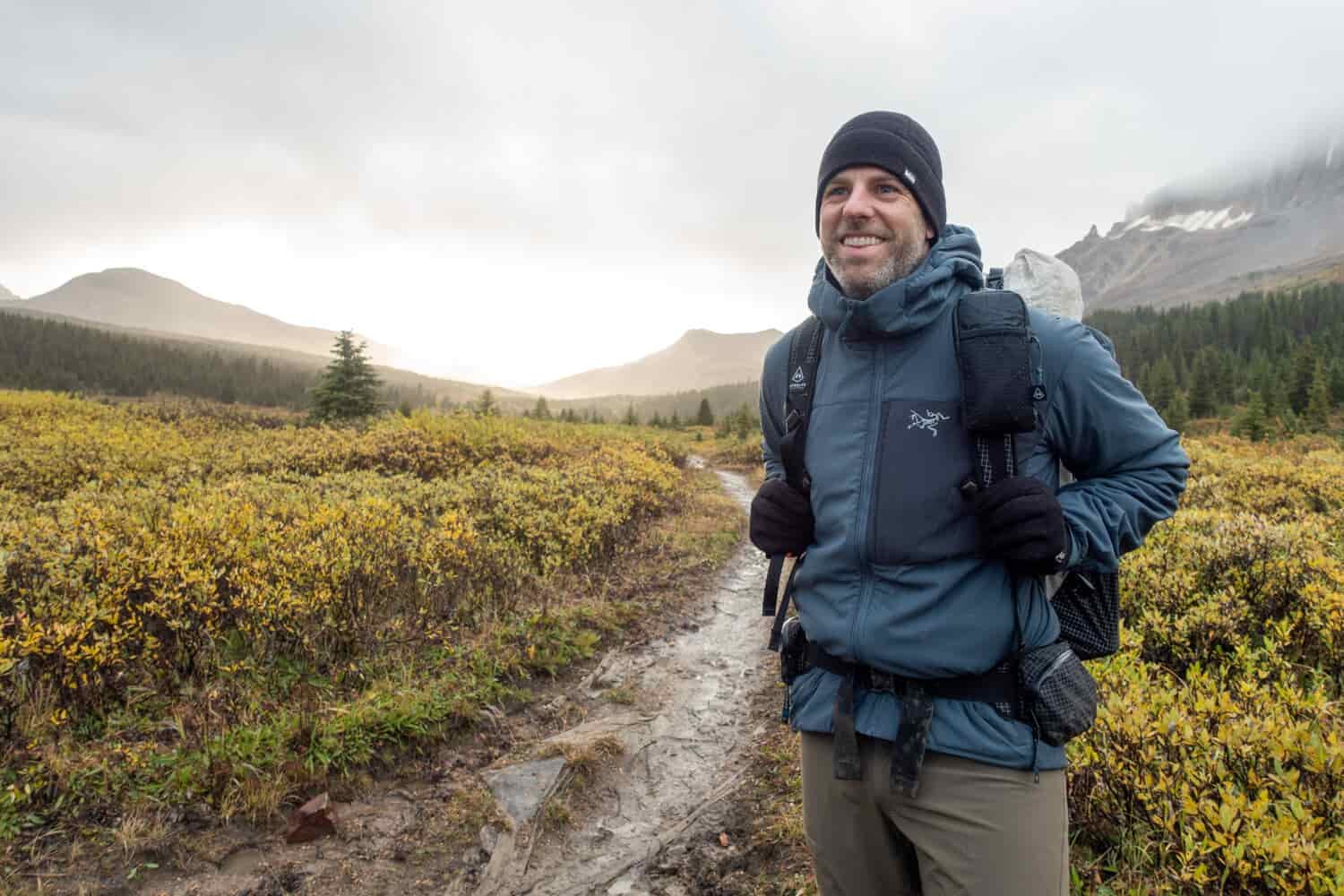 A-backpacker-wearing-the-Arcteryx-Proton-LT-Hoody on a wet and muddy trail