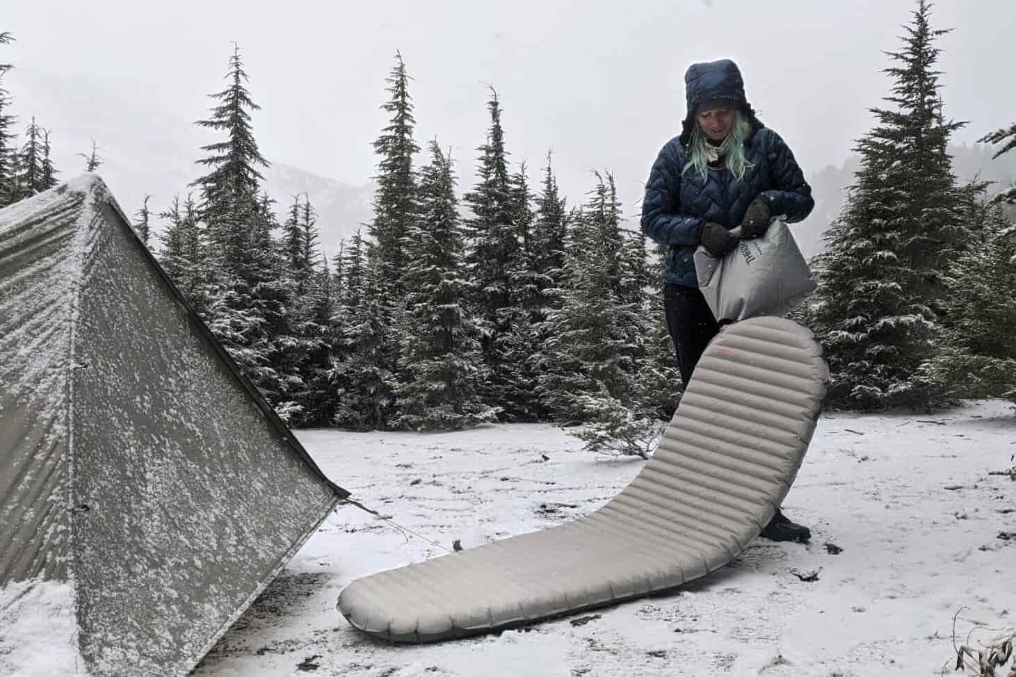 A hiker using a pump sack to inflate the Therm-a-Rest-NeoAir-XTherm sleeping pad on a snowy backpacking trip