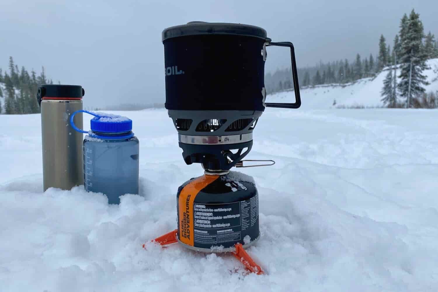 Closeup-of-the-Jetboil-Mini-Mo-Stove-a-Nalgene-Water-Bottle-and-a-Lightweight-Hydroflask-in-the-snow