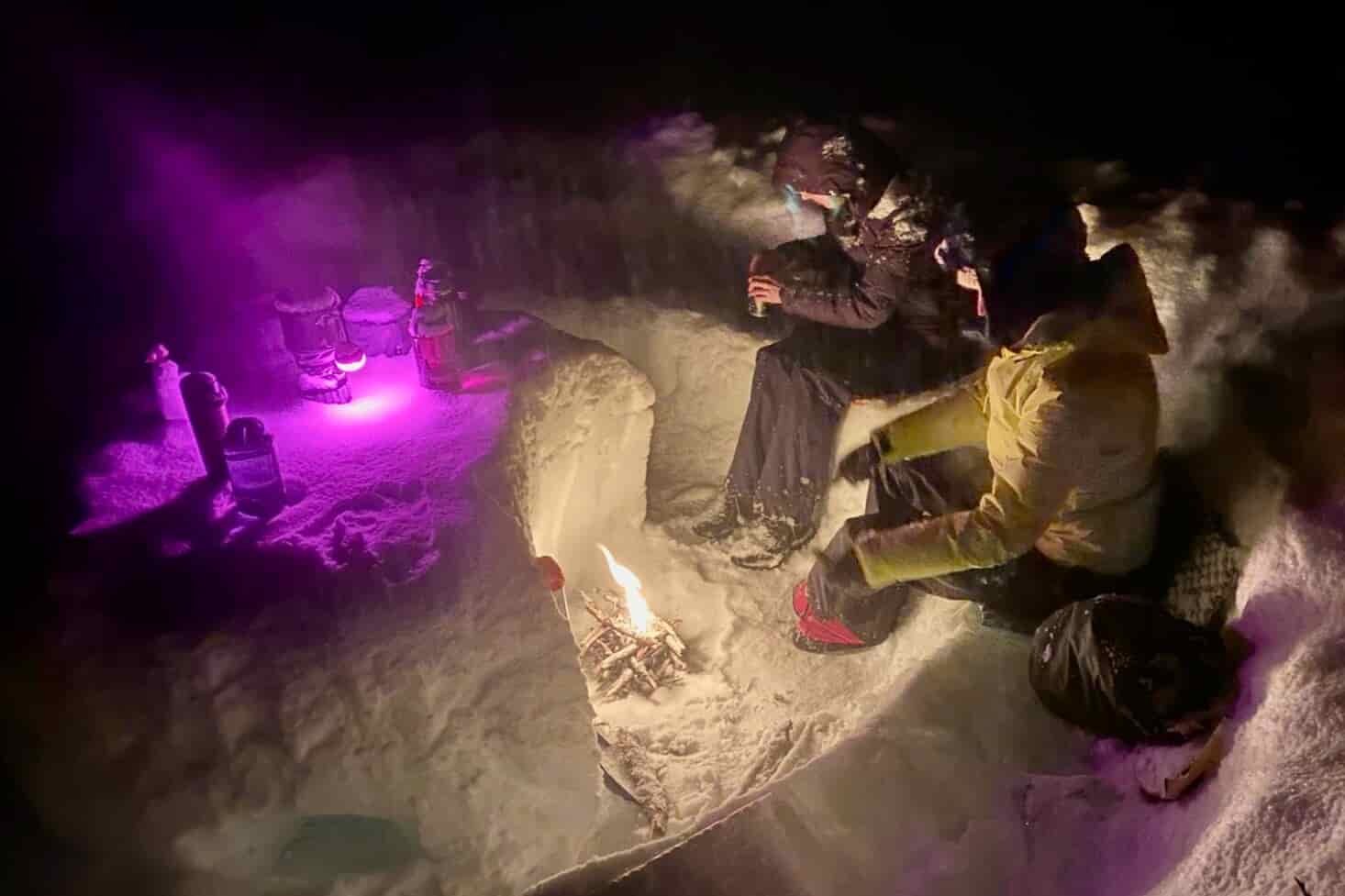 Hikers gathering around a fire at night on a winter camping trip