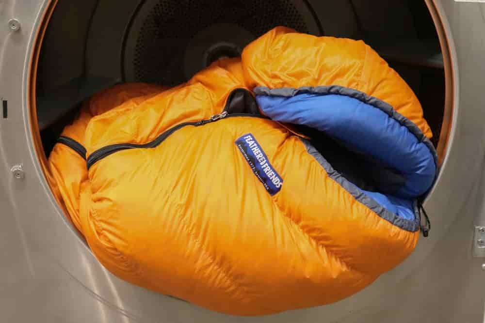 An orange Feathered Friends down sleeping bag spills out of a front-loading dryer clean, dry, and ready to use