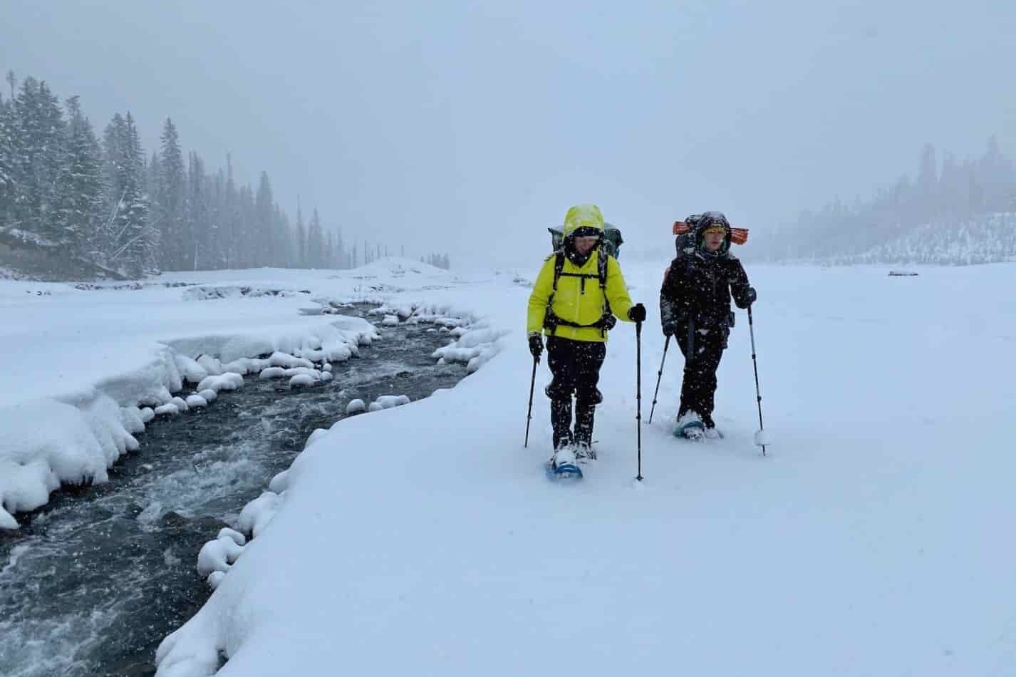Snowshoeing beside a flowing river in the winter. The snowshoers are carrying backpacking packs to camp.