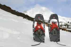 THE MSR LIGHTNING ASCENT SNOWSHOES with their heels stuck in the snow on a snowy slope with a mountain in the background