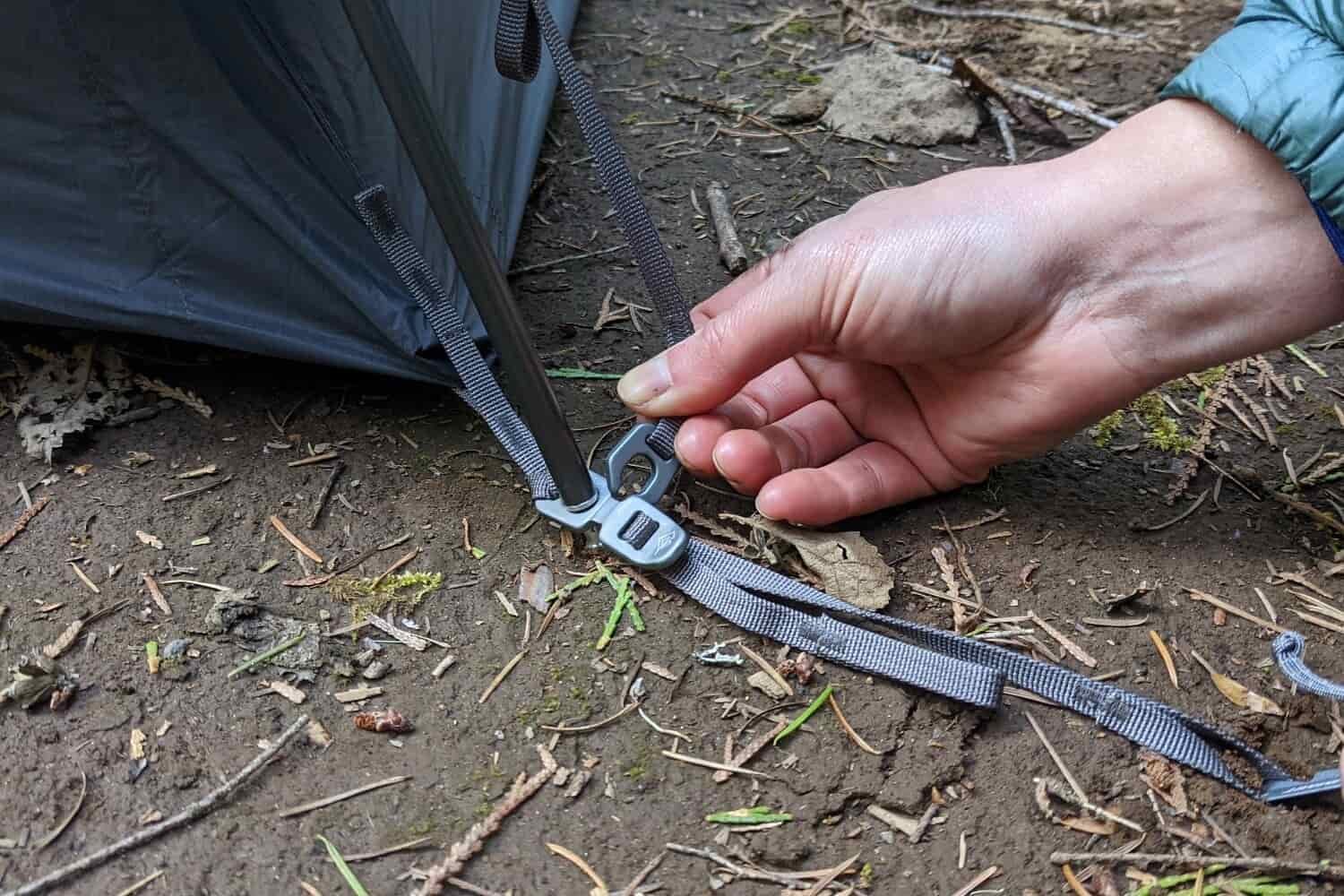 A hiker's hand attaching the Quick Connect clip on the rainfly of the Sea to Summit Telos TR2 backpacking tent to the pole seat