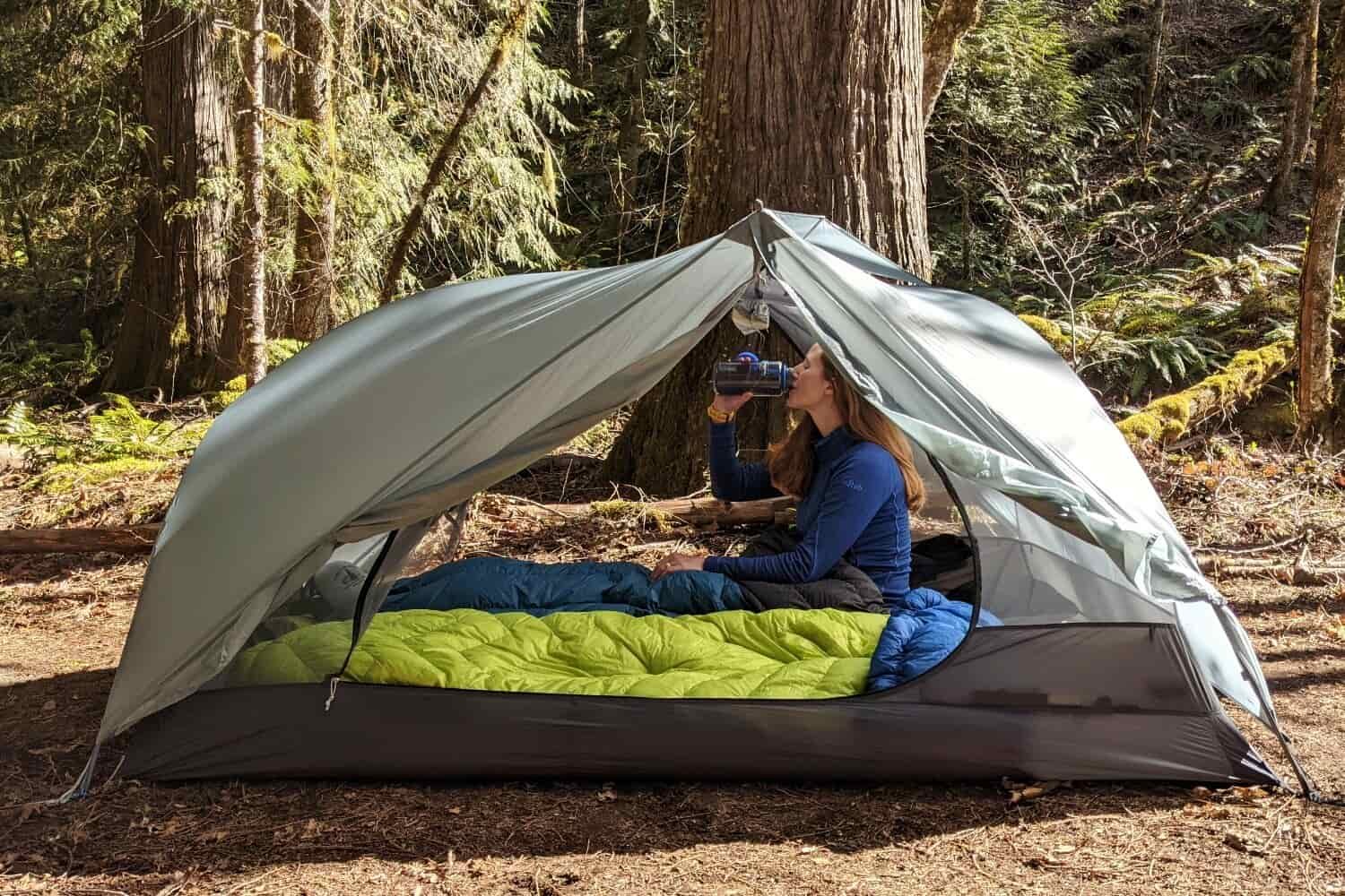 a backpacker sitting up inside their telos TR2 tent drinking out of a nalgene