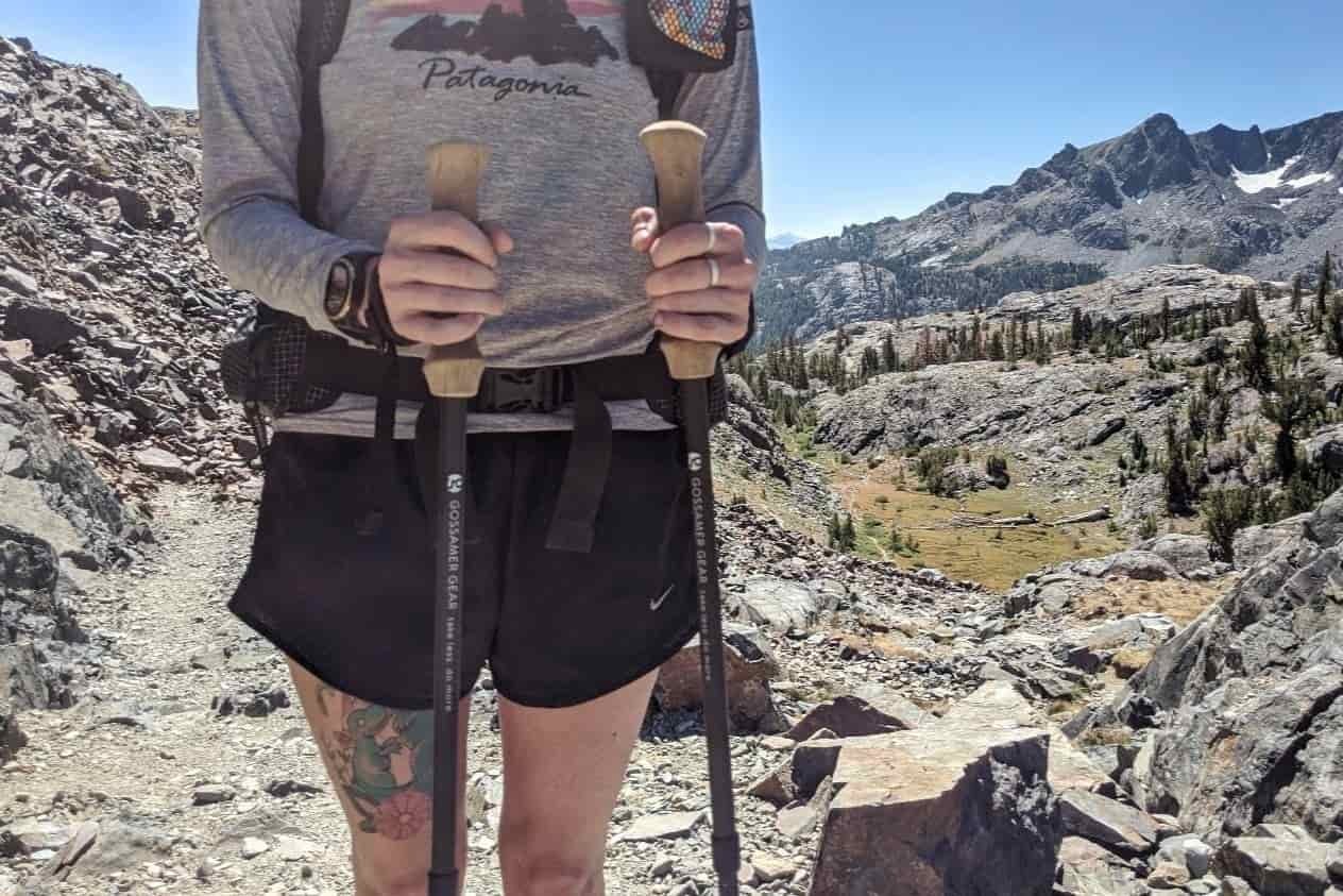 Close up shot of a hiker holding trekking poles on a rocky trail in the mountains