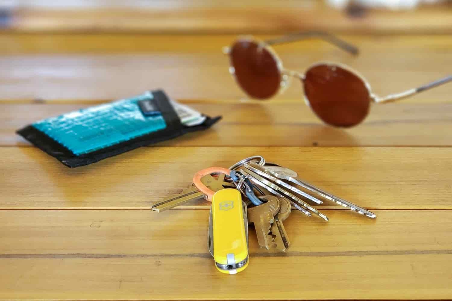 A hiker's cards, sunglasses, and key ring with a Swiss army knife sit on a wooden table