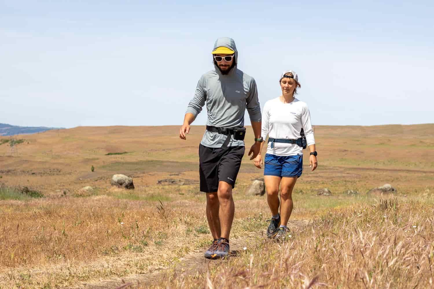 A male and female hiker in sun shirts hike across an exposed plain
