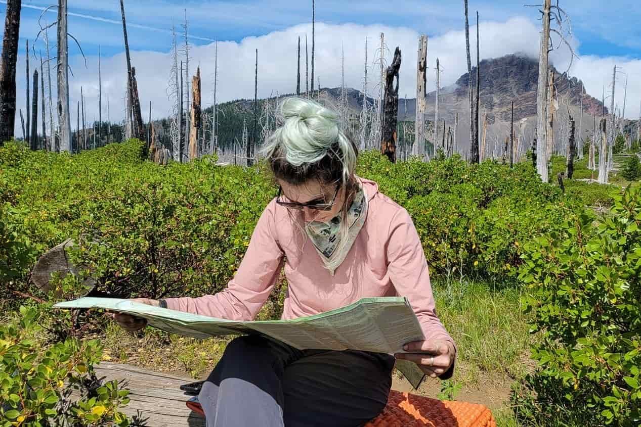 A female hiker sits on a bench while consulting her map of the trail