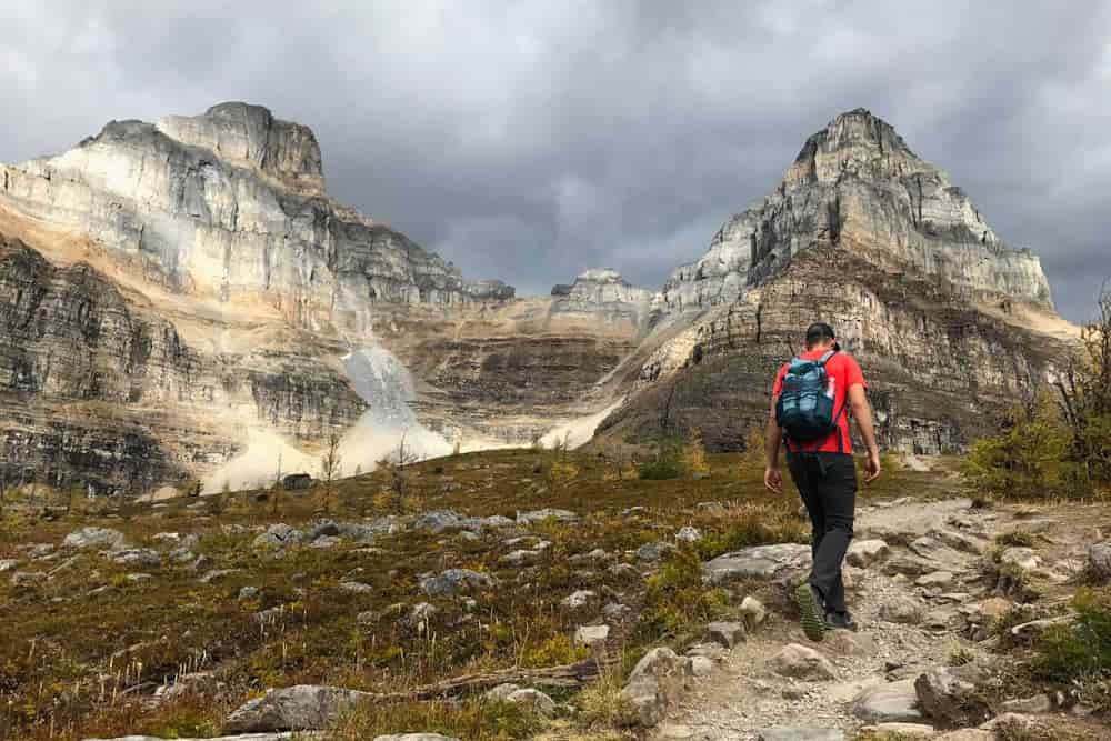 A male hiker heads up a rocky trail in the mountains with a loaded day pack