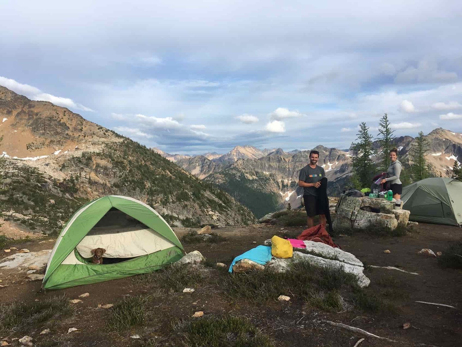 two backpackers setting up camp with a puppy poking its head out of one of the tents in the north cascades wilderness in washington