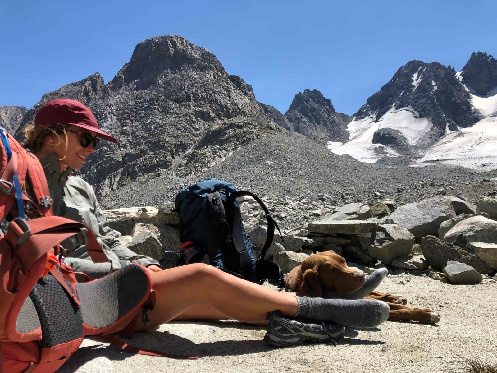 a backpacker resting on the ground with a dog resting its head on her foot in the wind river range