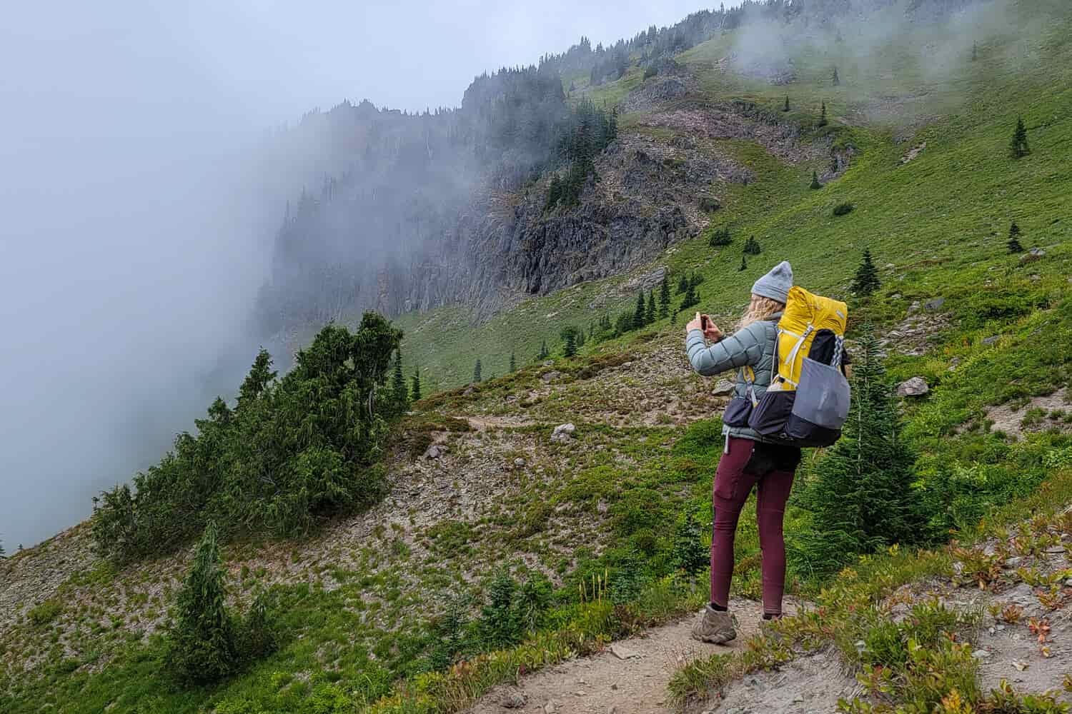 A female hiker shoots a landscape photo with her cellphone while hiking on a ridge