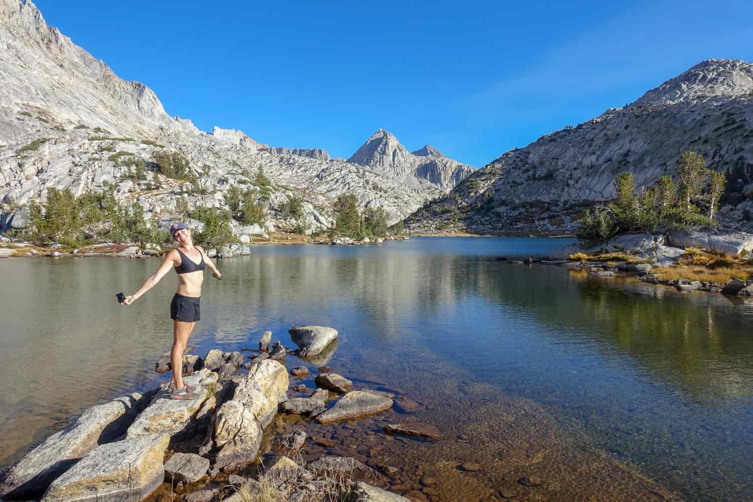 A female hiker poses on the shoreline of an alpine lake