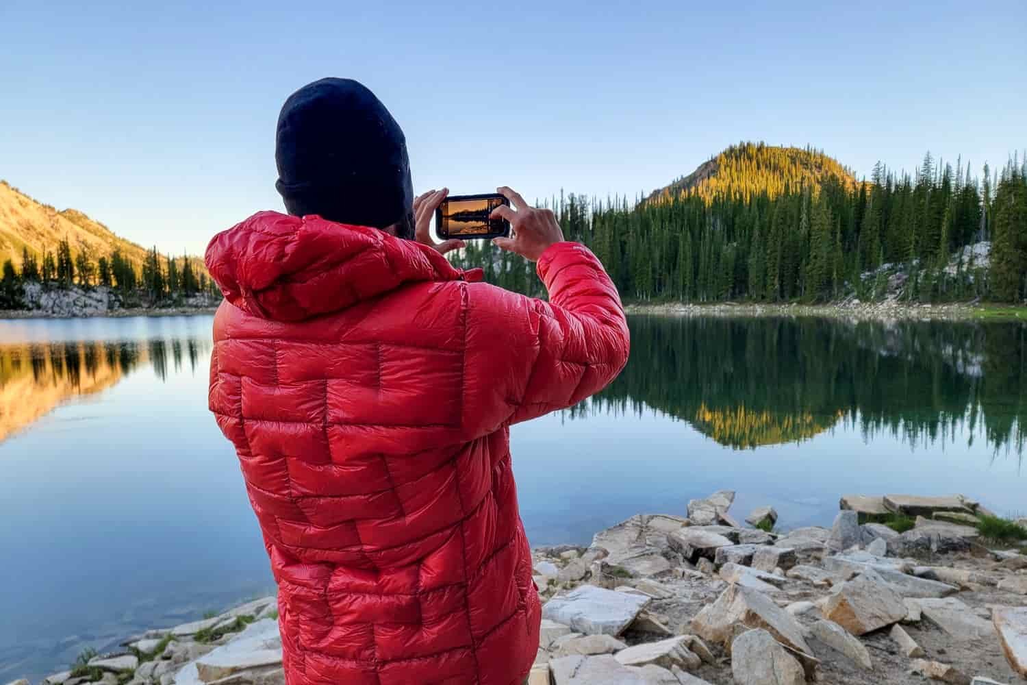 A hiker lines up a cellphone photograph of a mountain lake