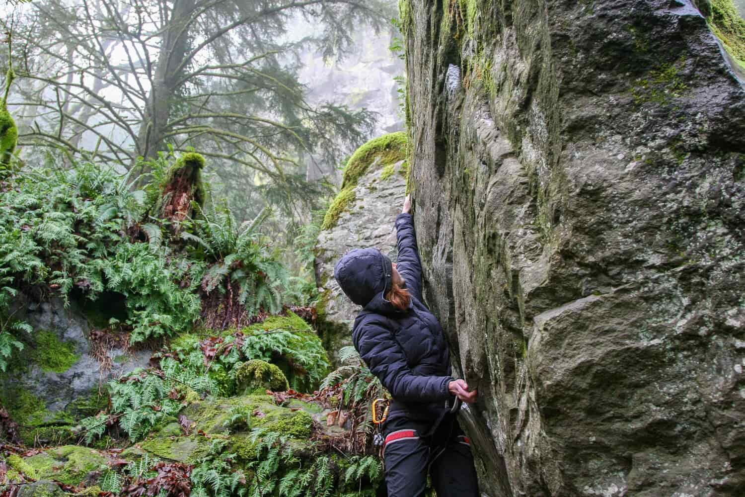 A natural-looking photography of a women climber reaching for a handhold on a gray cliff face