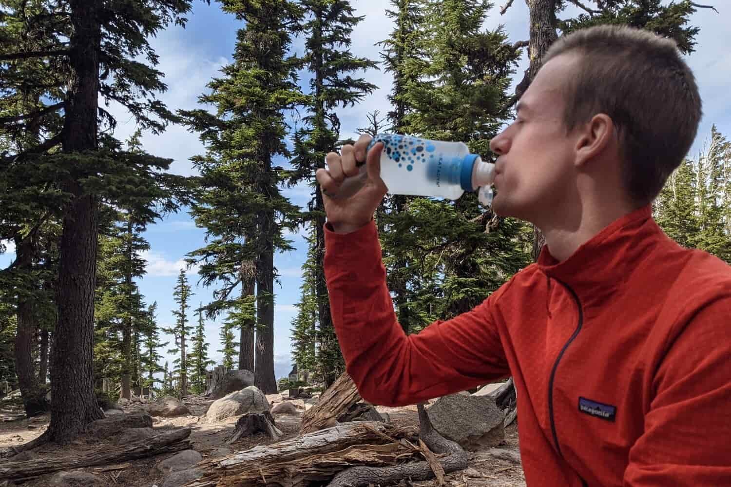 backpacker uses one hand to squeeze their untreated water through a filter inside the bottle and then into their mouth.
