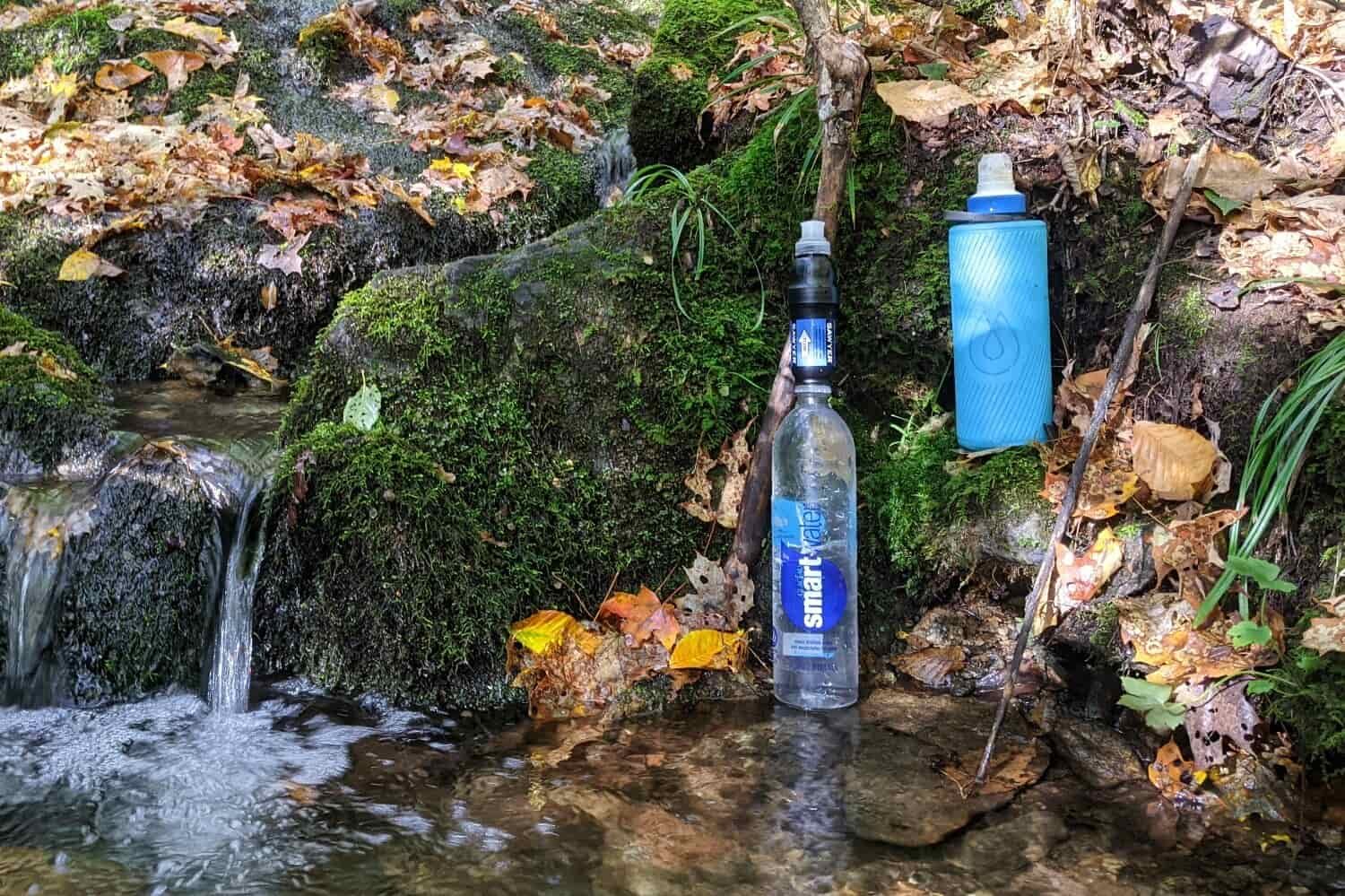 two water filters beside a stream attached to water bottles for backpacking