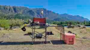 The GCI Outdoors Master Cook Station set up in a lakeside campsite with the Camp Chef Everest 2x stove, a cookset, a YETI Tundra Cooler, lantern, etc.