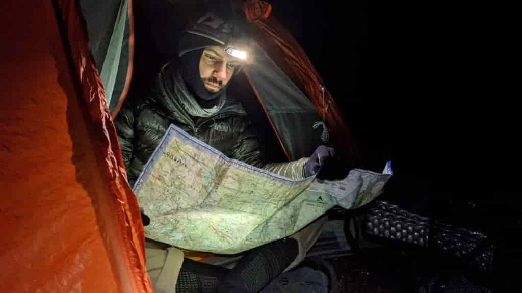 a backpacker is reading a map while bundled up seated at the door of his tent