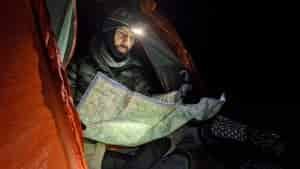 a backpacker is reading a map while bundled up seated at the door of his tent