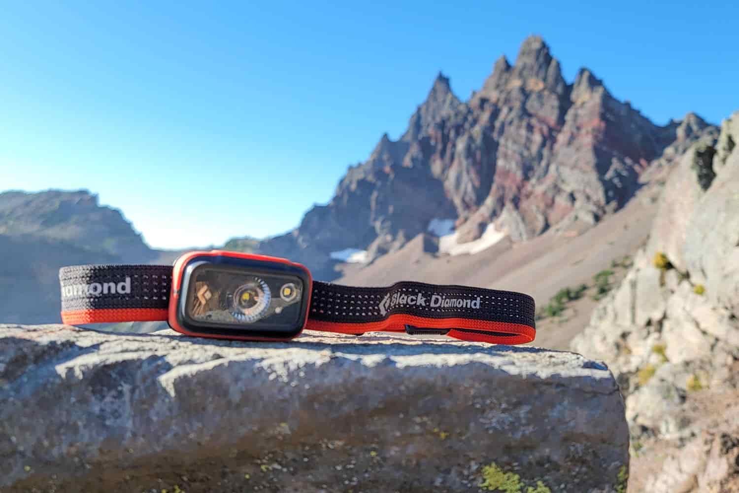 the black diamond spot 400 is a rechargeable headlamp placed on a rock near broken top in oregon on a sunny day