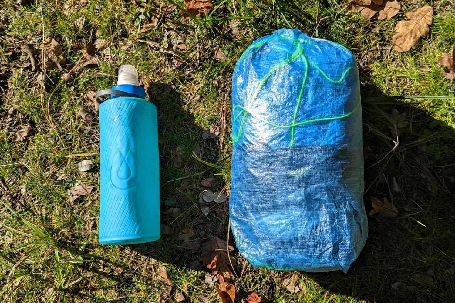 the zpacks plex solo tent packed in a compression sack displayed next to a one liter water bottle to compare size