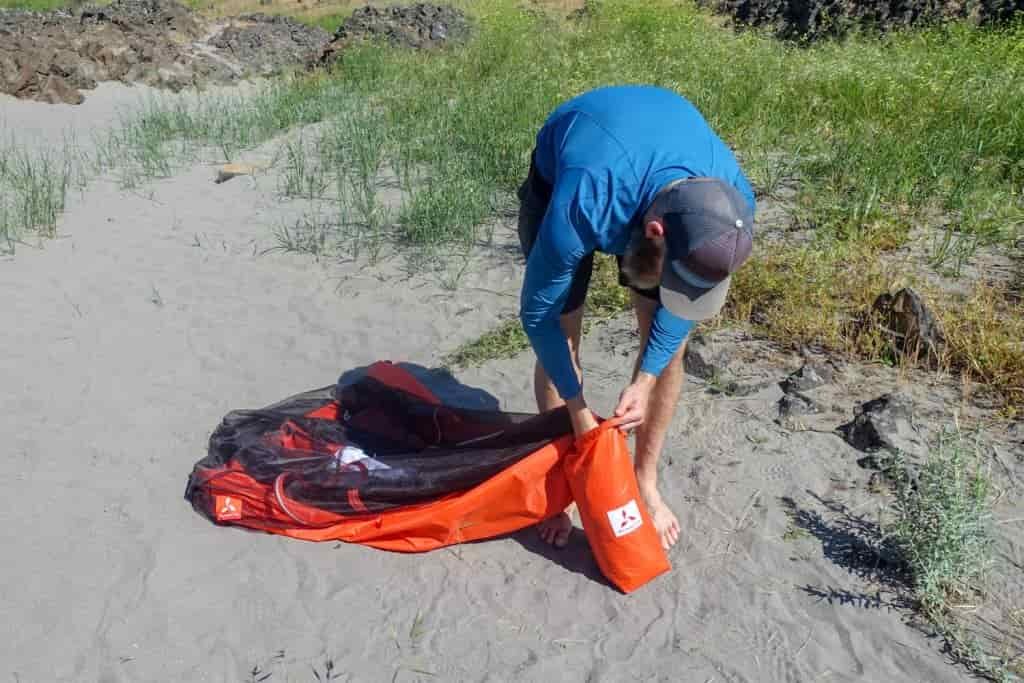 person stuffing tent into stuff sack
