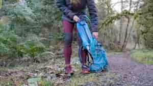 Waist-down view of a female hiker pulling the Gregory 3D Hydro hydration bladder out of her backpack along a trail