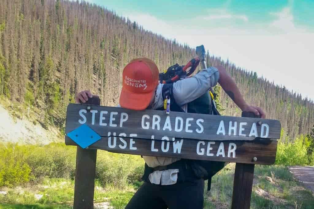 A hiker leans on a sign that warns about steep terrain ahead