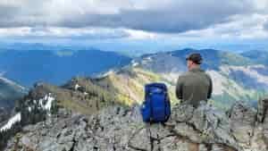 A hiker sitting next to the REI Trail 25 daypack on a mountain ridge