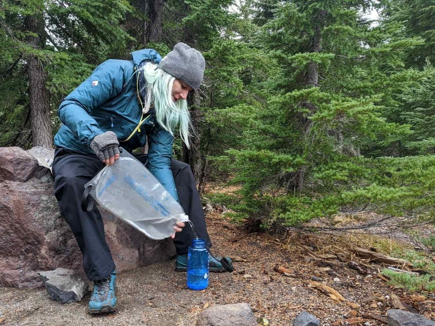 a backpacker in Oregon pour clean drinking water from their platypus gravityworks filter to a nalgene bottle